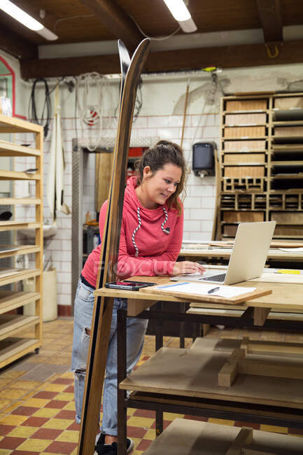 Женщина в мастерской, с ноутбуком, лыжи опирается на прилавок рядом с ней — стоковое фото