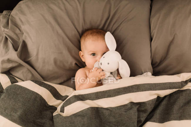 Porträt eines kleinen Mädchens, das mit Spielzeugkaninchen im Bett liegt — Stockfoto
