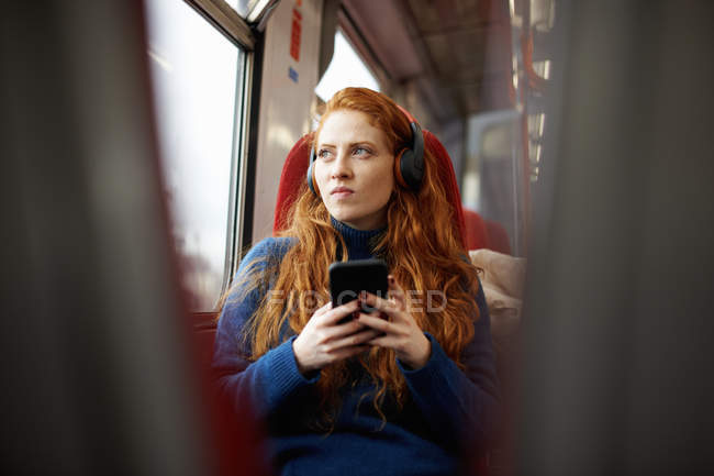 Mujer en tren escuchando música con teléfono móvil - foto de stock