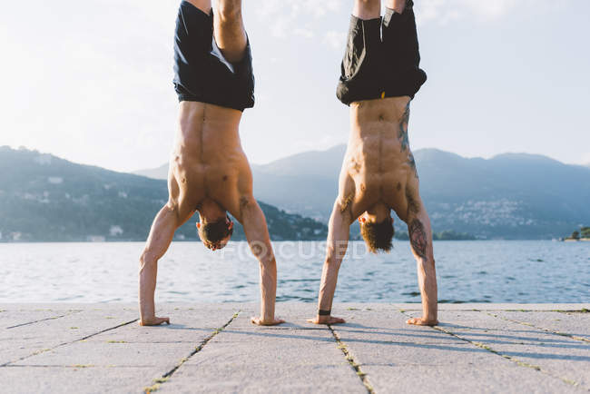 Двое молодых людей, делающих подставки на берегу озера Комо, Ломбардия, Италия — стоковое фото