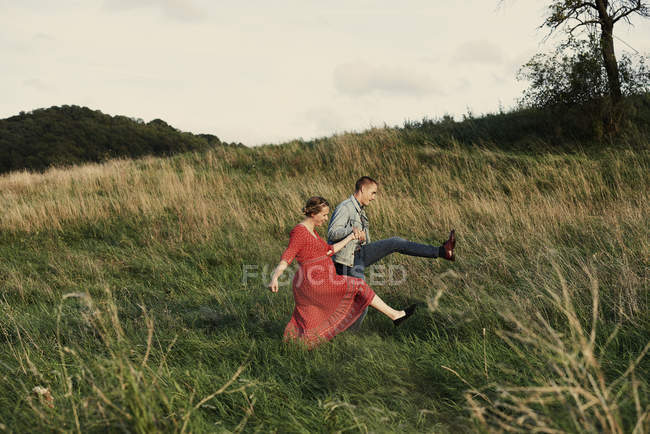 Fun pregnant couple marching in field — Stock Photo