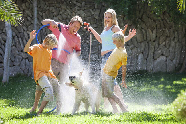 Family spraying dog with water from hosepipe — Stock Photo