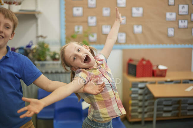 Primaire écolière et garçon amusant autour dans salle de classe — Photo de stock