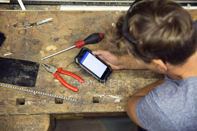 Overhead view of man in workshop using smartphone — Stock Photo