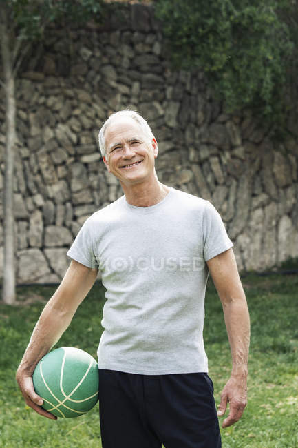 Портрет чоловік тримає баскетбол, дивлячись на камеру посміхається — стокове фото