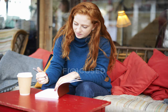 Mujer en la cafetería escribiendo en bloc de notas - foto de stock