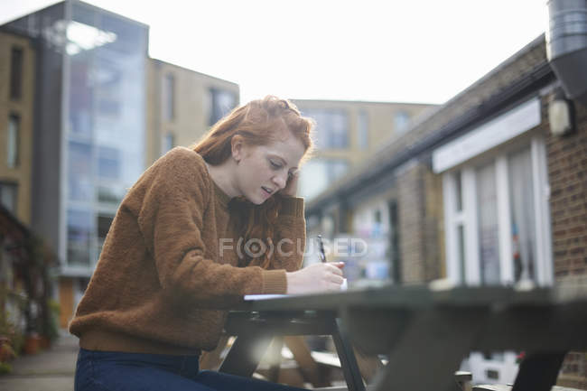 Frau sitzt an Picknickbank und schreibt — Stockfoto