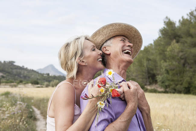 Couple dans le champ avec bouquet de fleurs étreignant et souriant — Photo de stock