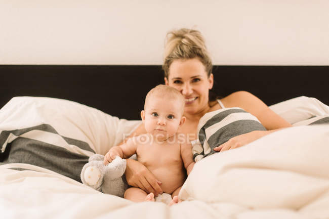 Retrato de mulher deitada na cama com bebê filha — Fotografia de Stock