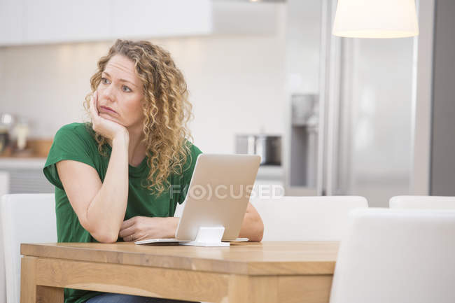 Mulher sentada na mesa da cozinha com laptop — Fotografia de Stock