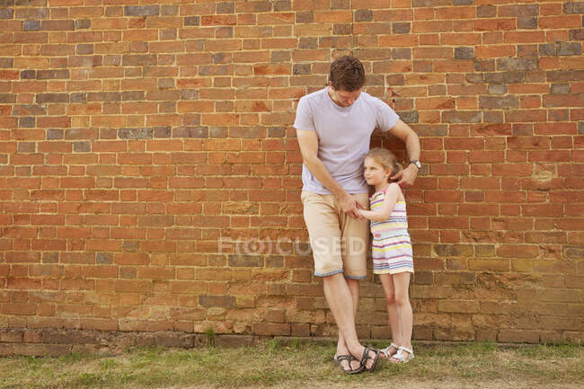 Menina e pai encostados contra a parede de tijolo — Fotografia de Stock