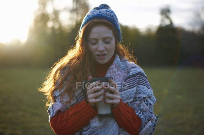 Молодая женщина, завернутая в одеяло с горячим напитком — стоковое фото
