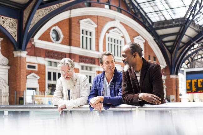 Трое взрослых мужчин на вокзале, стоя вместе, разговаривая — стоковое фото