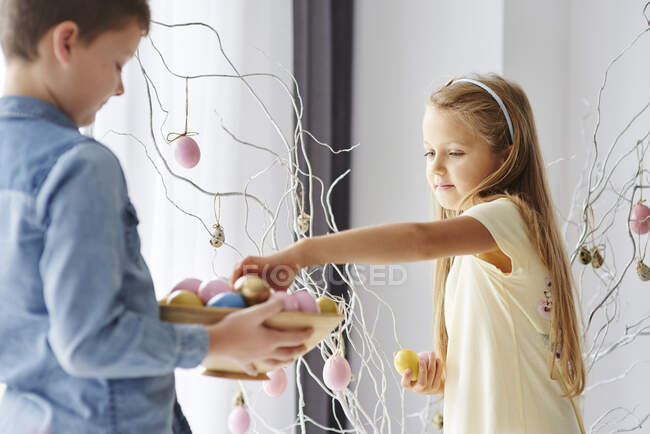 Дівчина і брат прикрашають гілки барвистими великодніми яйцями — стокове фото