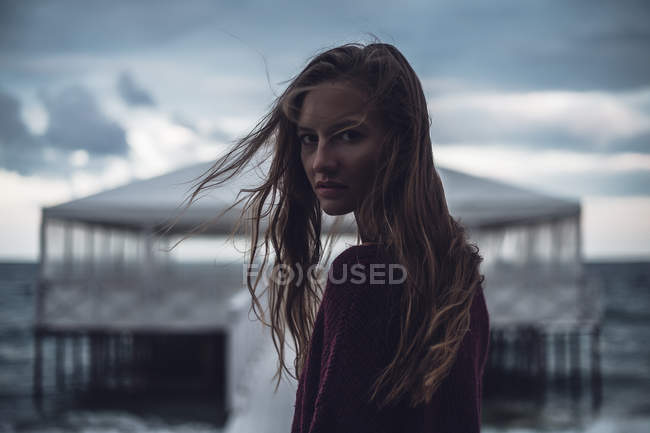 Portrait of young woman with flyaway hair on pier at dusk — Stock Photo