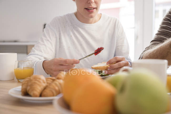 Cropped shot of young woman and boyfriend having croissants at breakfast table — Stock Photo