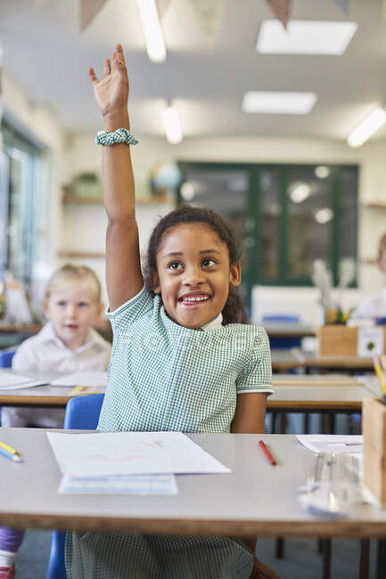 Schoolgirl with hand up in classroom at primary school — Stock Photo