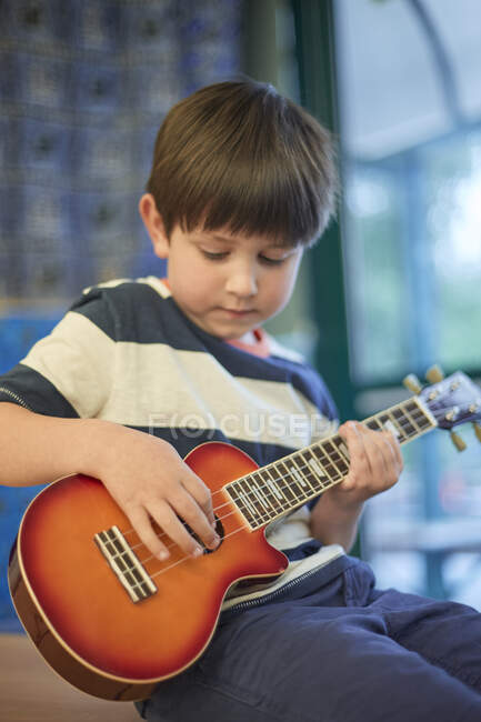 Schoolboy playing ukulele  in classroom at primary school — Stock Photo