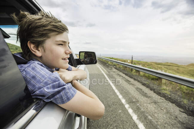 Rapaz em viagem de carro inclinado para fora da janela do carro — Fotografia de Stock
