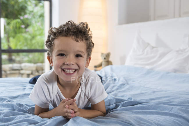 Мальчик лежит на кровати и улыбается в камеру — стоковое фото