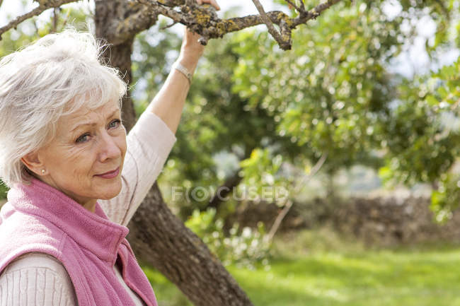 Portrait of senior woman in garden, holding tree branch — Stock Photo