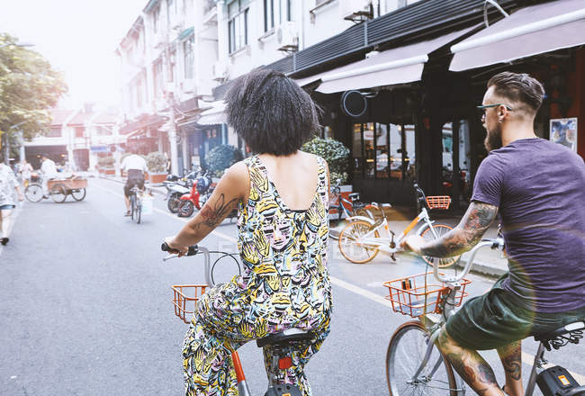 Multi ethnic hipster couple cycling along city street, Shanghai French Concession, Shanghai, China — Stock Photo