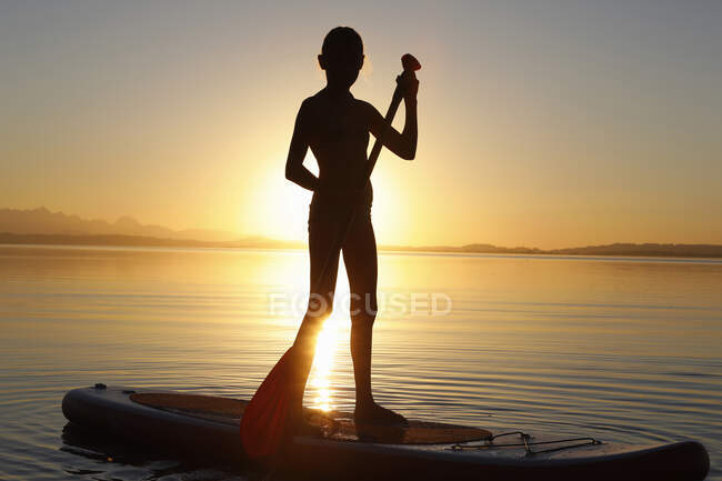 Young girl paddle boarding on water, at sunset — Stock Photo