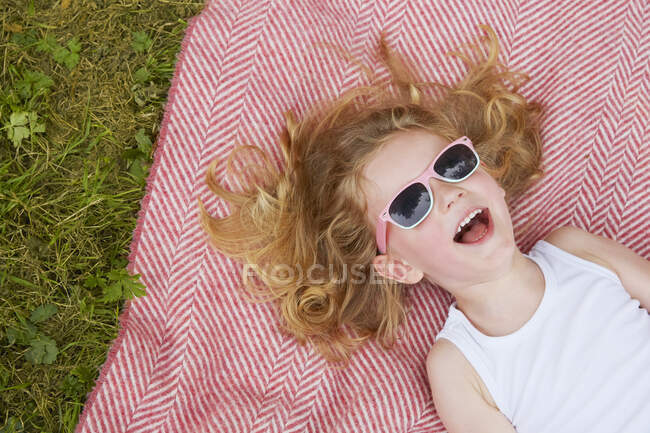 Overhead portrait of girl with blond hair and sunglasses posing on blanket — Stock Photo