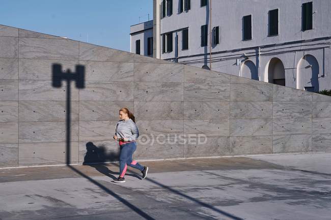 Curvaceous young female runner running along sidewalk — Stock Photo