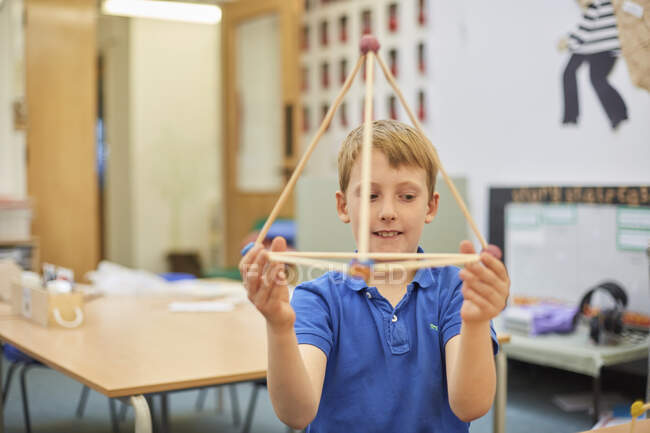 Primary schoolboy holding up plastic straw pyramid in classroom — Stock Photo