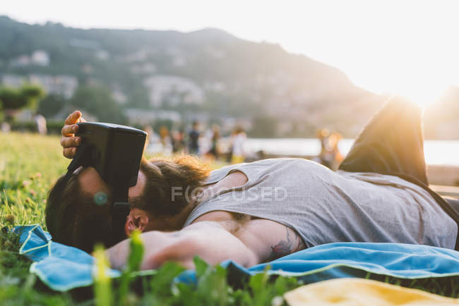 Молодой мужчина на траве с гарнитурой виртуальной реальности, озеро Комо, Ломбардия, Италия — стоковое фото