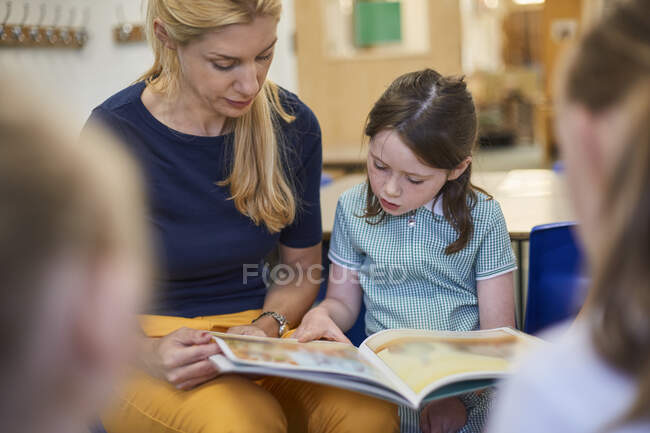 Teacher with schoolgirls reading storybook in classroom at primary school — Stock Photo