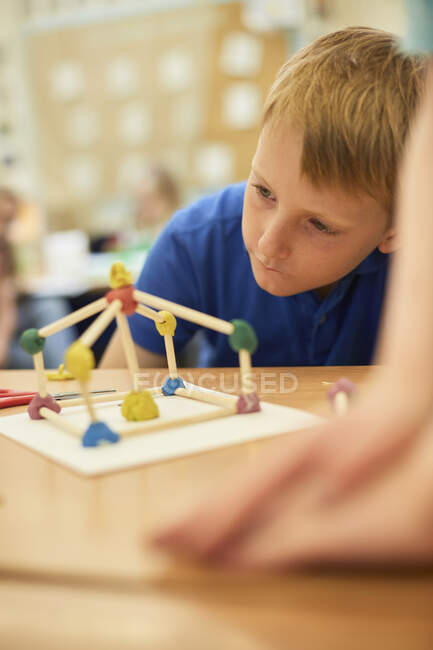 Colegial de primaria mirando el modelo de paja de plástico en los escritorios del aula - foto de stock
