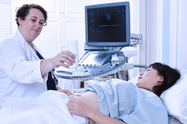 Sonographer applying gel to pregnant patient stomach — Stock Photo