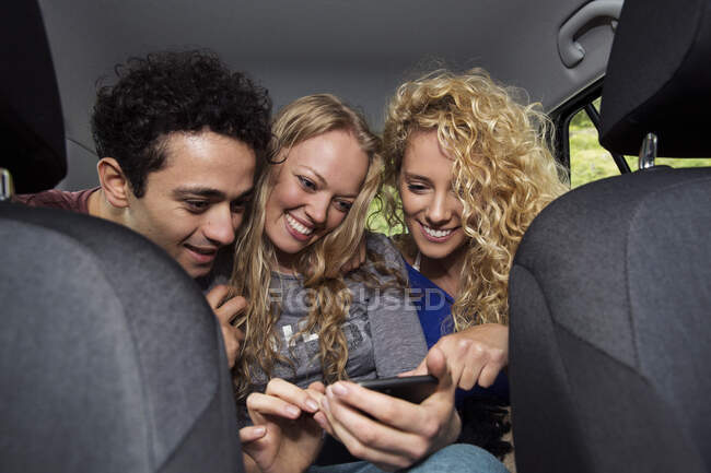 Amigos en el asiento trasero del coche mirando el teléfono inteligente - foto de stock