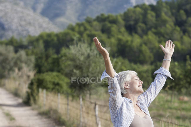 Senior woman, outdoors, arms raised, carefree expression — Stock Photo