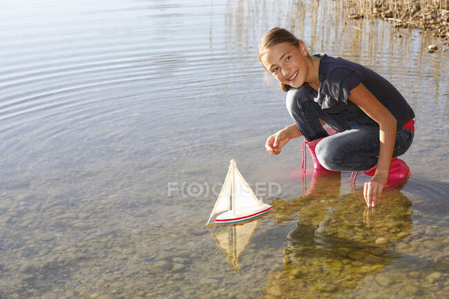 Chica joven flotante juguete barco en el agua - foto de stock