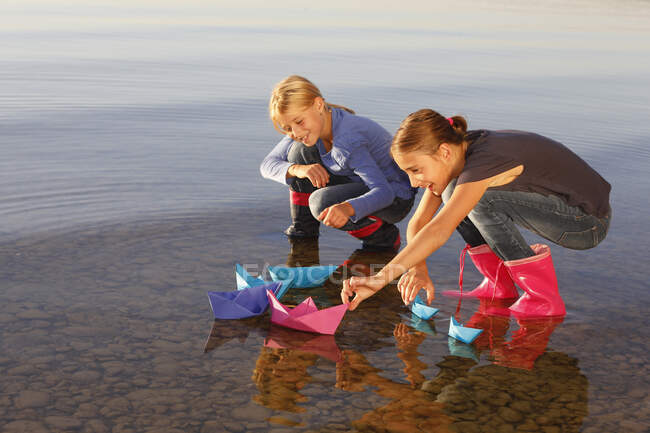Две молодые девушки плавают на бумажных лодках по воде — стоковое фото