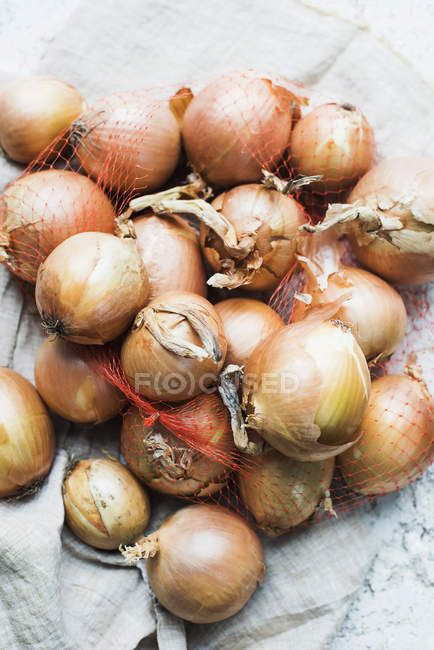 Vista superior de cebollas en bolsa de red en tela - foto de stock