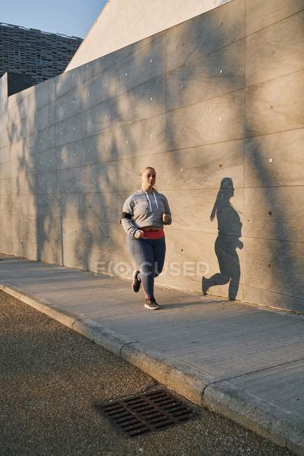 Изогнутая молодая женщина бежит по тротуару — стоковое фото