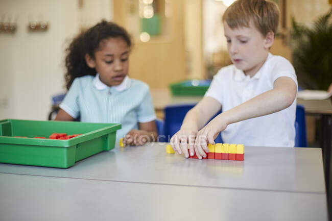 Colegial y niña construyendo bloques de juguetes en el aula de la escuela primaria - foto de stock