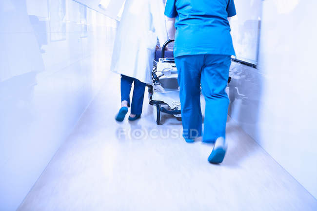 Cropped rear view of doctors pushing stretcher in corridor — Stock Photo