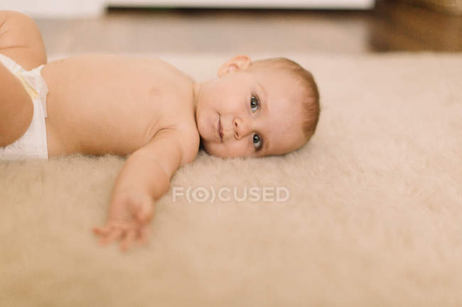 Porträt eines süßen Mädchens in Windel, das auf beigem Teppich liegt — Stockfoto