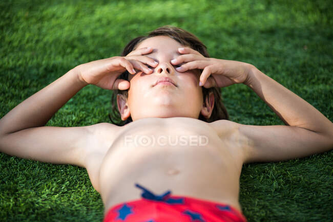 Garçon couché sur l'herbe couvrant les yeux — Photo de stock