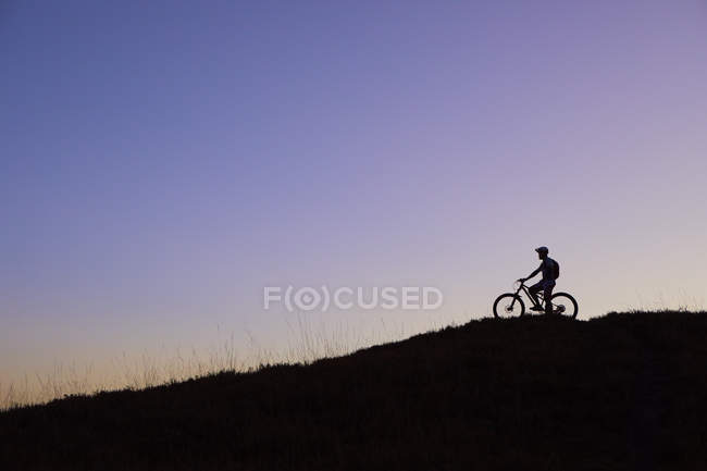 Silhouette eines Mountainbikers, der den Sonnenuntergang vom Hügel aus betrachtet — Stockfoto