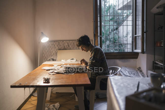 Jovem artista desenhando em caderno de esboços na mesa em estúdio — Fotografia de Stock