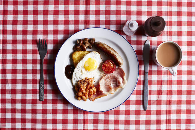 Full English breakfast on checked table cloth, overhead view — Stock Photo
