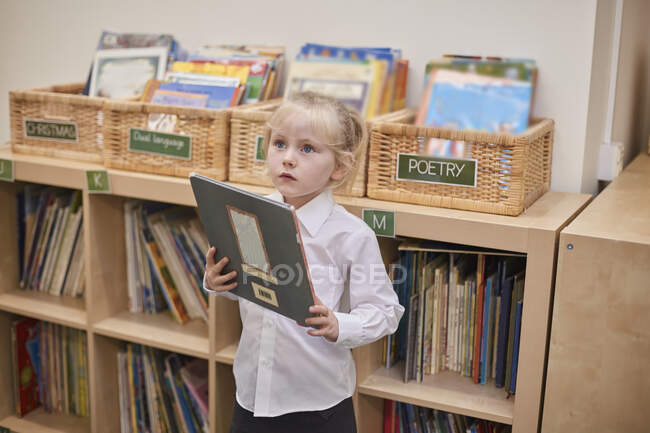 Graziosa studentessa holding book in aula presso la scuola primaria — Foto stock