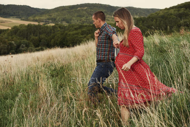 Pregnant couple strolling down on hillside — Stock Photo