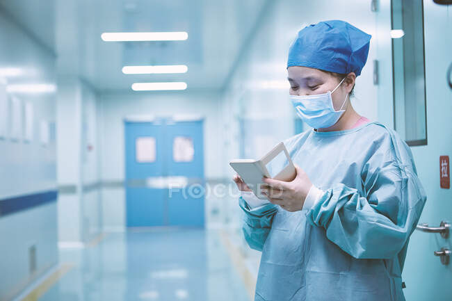 Женщина-хирург смотрит на смартфон в операционном коридоре родильного отделения — стоковое фото